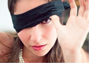photo of a woman peeking out from under a black blindfold