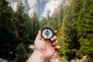 photo of a hand holding a compass with a mountain scene background (by Devon Luongo)