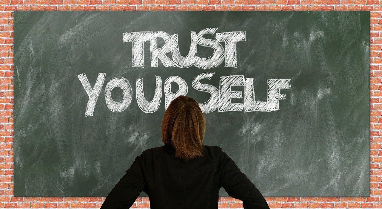 photo of woman facing a black board with the words "trust yourself"