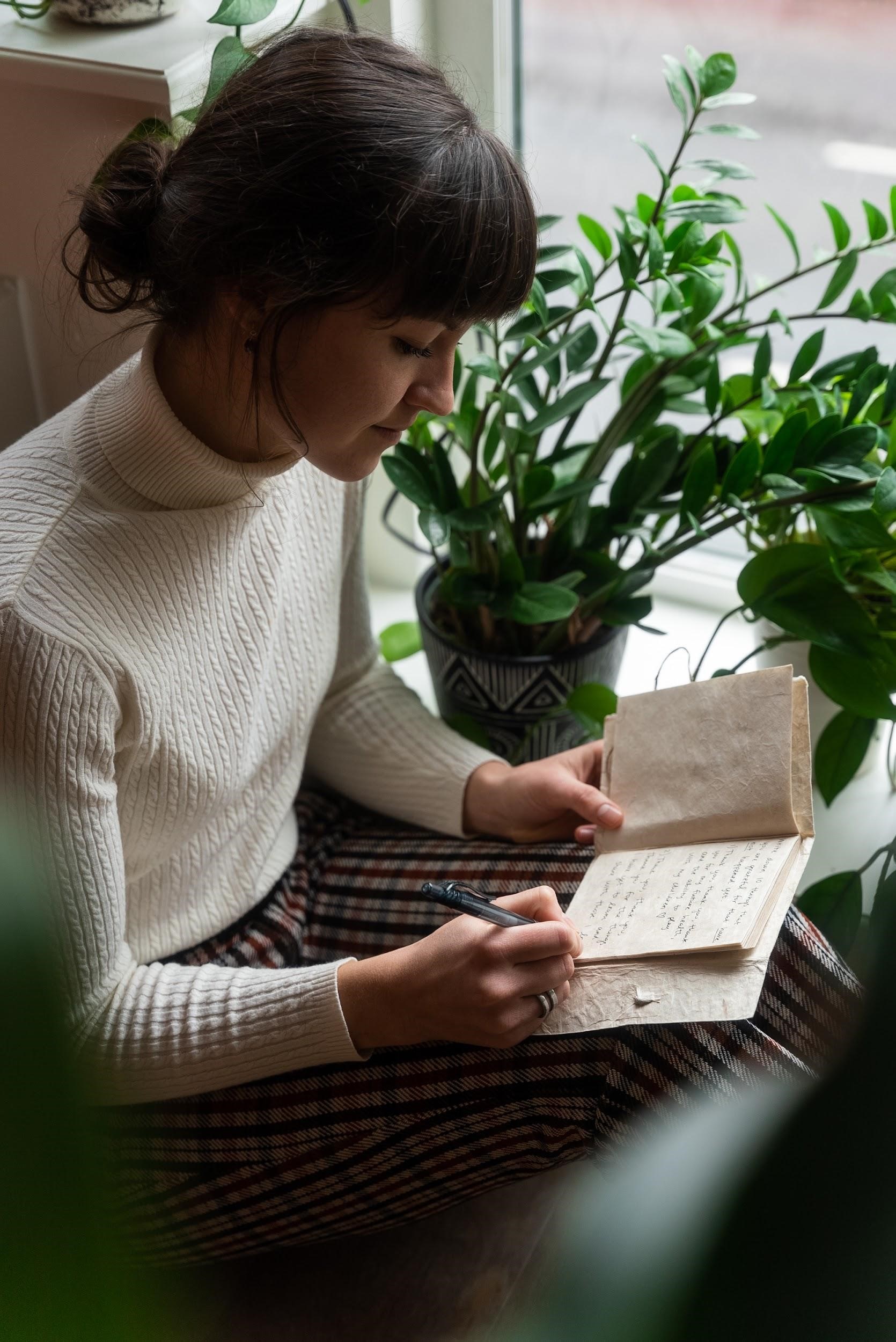 photo of a young woman sitting by a window and writing in a journal