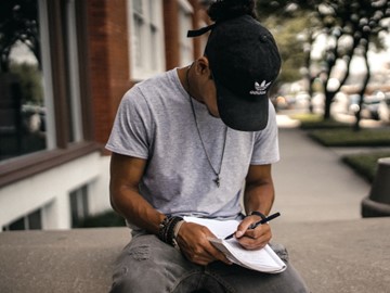 photo of a man writing while sitting outside