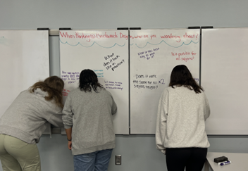 Three students writing on a white board as part of the I Wonder activity